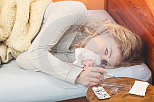 Sick woman in bed sneezing in tissue.