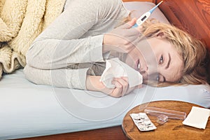 Sick woman in bed sneezing in tissue.