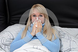 Sick woman blowing her nose in bed