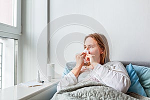 Sick woman blowing her nose with headache and fever lying under the blanket. Sick woman staying in bed with temperature durong