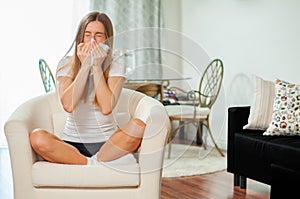 Sick woman blowing her nose at home in the living room