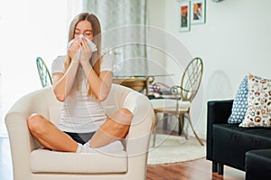 Sick woman blowing her nose at home in the living room