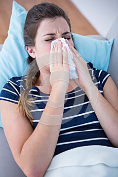 Sick woman blowing her nose lying on couch