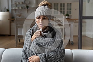 Sick woman covered with blanket caught cold, sitting on couch