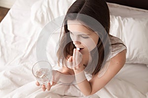 Sick woman drinking pill in bed in the morning