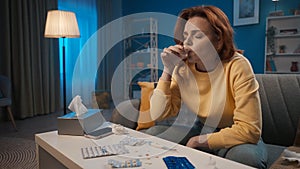 A sick woman drinks cough syrup, antipyretic or antiinflammatory. A woman is sitting in the living room on a sofa in photo