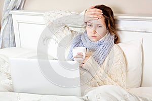 Sick woman feeling bad, resting and working with her laptop and internet in her bed at home