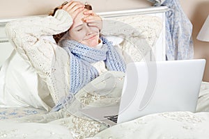 Sick woman feeling bad, resting and working with her laptop and internet in her bed at home