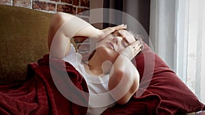 Sick woman feeling unwell having headache lying on sofa and massaging head. Healthcare, female feeling sick at home, illness and
