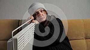 Sick woman feels cold and dresses warmly sitting near heater