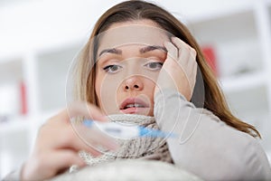 sick woman with fever checking temperature with thermometer