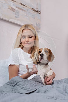 sick woman holding container with medicine and hugging dog while sitting