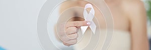 Sick woman holding pink ribbon in her hands in clinic closeup