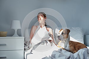 Sick woman with hurt arm in bed with a dog.