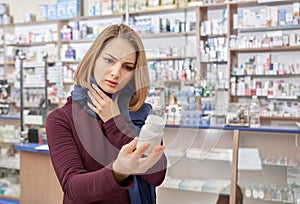 Sick woman looking at bottle mock with pills in drugstore.