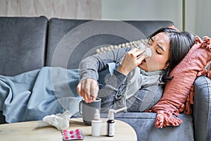 Sick woman lying on sofa at home, catching cold. Young girl freezing from heating problem in her apartment, concept of