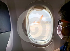 Sick woman passenger wear face mask and eyeglasses sit on passenger economy seat near cabin window inside airplane. Passenger