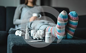 Sick woman resting on couch holding hot cup of tea. Ill person with flu, cold, fever or virus sitting on sofa at home in winter.