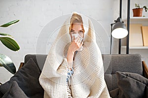 Sick woman sitting with kerchief under the blanket