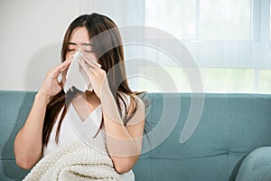 Sick woman sitting under blanket on sofa and sneeze with tissue paper in living