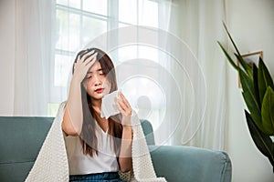 Sick woman sitting under blanket on sofa and sneeze with tissue paper in living room