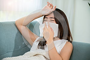 Sick woman sitting under blanket on sofa and sneeze with tissue paper in living room