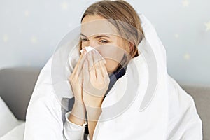 Sick woman sneezing holding tissue paper napkin sitting on couch at home