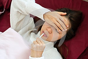 Sick woman with thermometer is lying in bed. She has cold, flu and high fever. concept of disease and ill