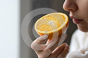 Sick woman trying to sense smell of half fresh orange, has symptom of Covid-19, loss of smell, taste photo