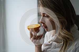 Sick woman trying to sense smell of half fresh orange, has symptom of Covid-19, loss of smell, taste