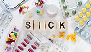 SICK. Word on wooden blocks on a desk. Medical concept with pills, vitamins, stethoscope and syringe on the background