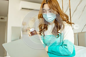 Sick young Asian woman hold medicine sit on couch use smartphone call to consult with doctor at home.Concept of telemedicine and