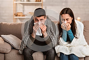 Sick young couple blowing noses sitting on couch, having flu