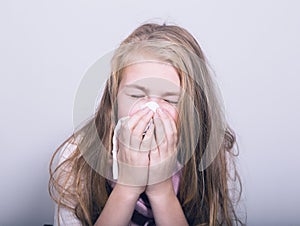 Sick young girl blowing her nose with paper tissue