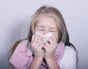 Sick young girl blowing her nose with paper tissue