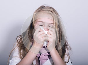 Sick young girl blowing her nose with paper tissue