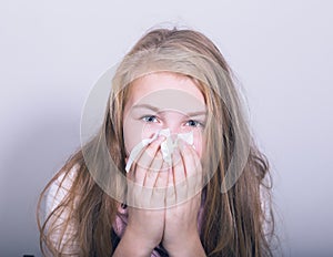 Sick young girl blowing her nose with paper tissue