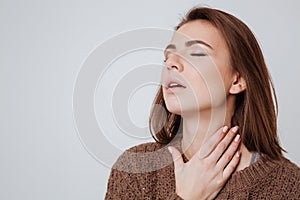 Sick young lady dressed in sweater touching her neck.