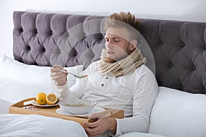 Sick young man eating soup to cure flu in bed