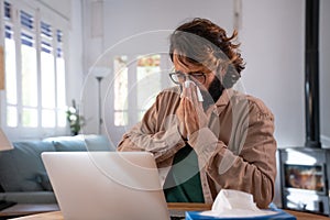 Sick young man snotting and working at home with laptop