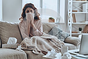 Sneezing just keep coming. Sick young women blowing her nose using facial tissues while sitting on the sofa at home photo