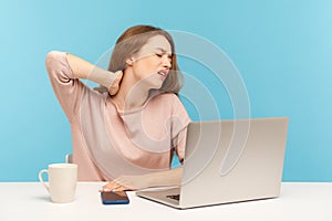 Sick young woman employee sitting at workplace with laptop feeling unwell with sore neck, hurting shoulders and back photo
