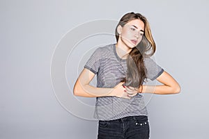 Sick young woman with heart attack, pain, touching her chest colored in red with hands isolated on gray background