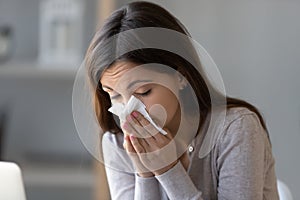 Sick young woman holding tissue and blowing her running nose photo