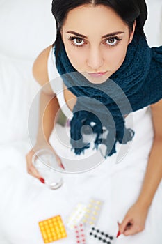 Sick young woman at home on the sofa, she is covering with a blanket, taking temperature and blowing her nose with a tissue