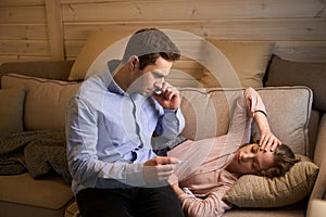 Sick young woman laying under warm blanket while man calling doctor