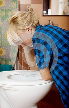 Sick young woman leaning on open toilet seat.