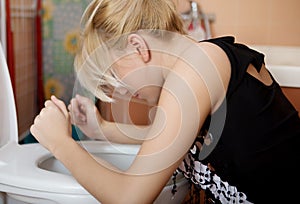 Sick young woman leaning on open toilet seat.