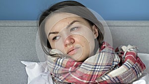 Sick young woman lies in bed and measures the temperature. She has a cough, chills, a runny nose. Flu, cold, or