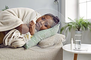 Sick young woman lying on sofa, wrapped in plaid, trying to warm herself